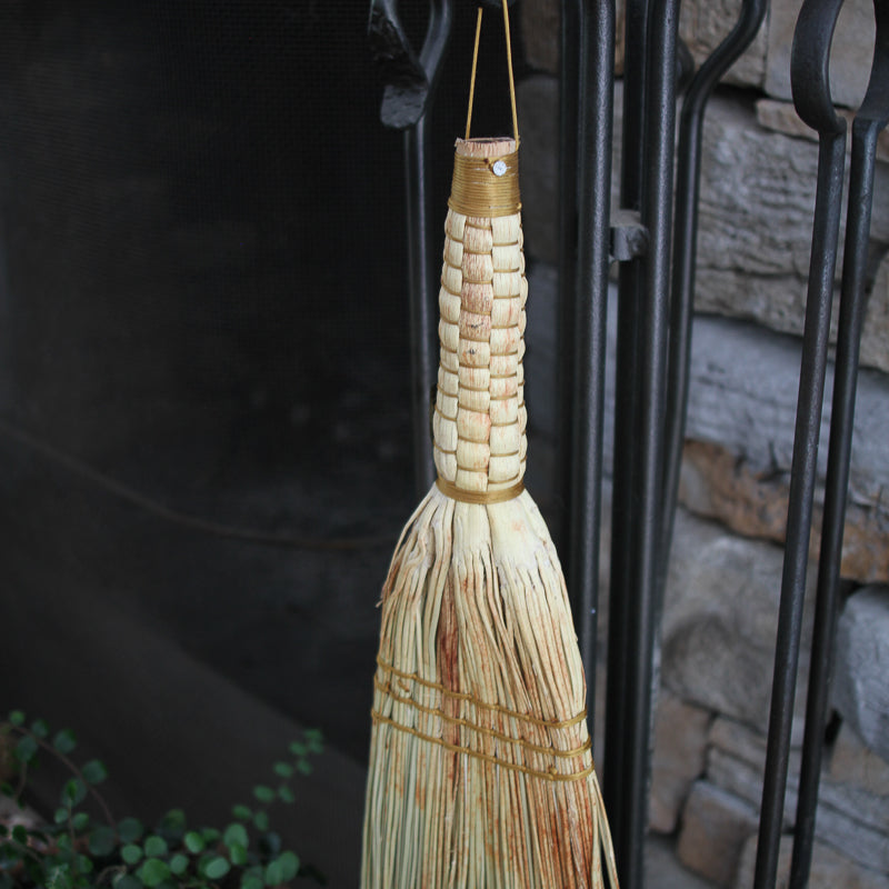 Woven broom hanging against a stone wall and metal gate background