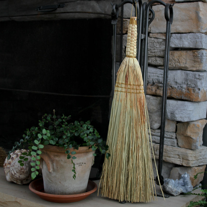 Broom leaning against a stone fireplace with a potted plant nearby
