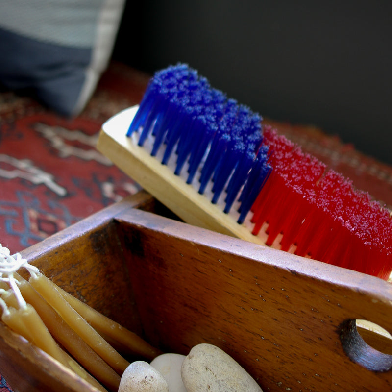Red and blue brush in a wooden box with pebbles and stones on a patterned surface.